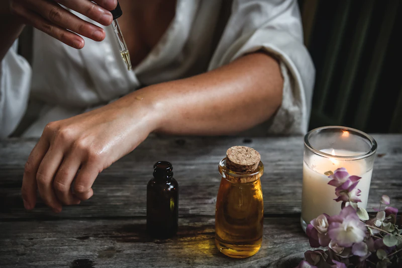 Massagetherapeut brengt warme olie aan op een arm, naast een brandende kaars